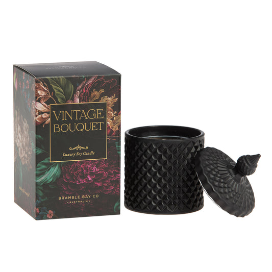 A black, textured Bramble Bay Co scented candle from Bramble Bay Co's Vintage Bouquet collection, with a geometric pattern on the container, displayed next to its floral-themed packaging.