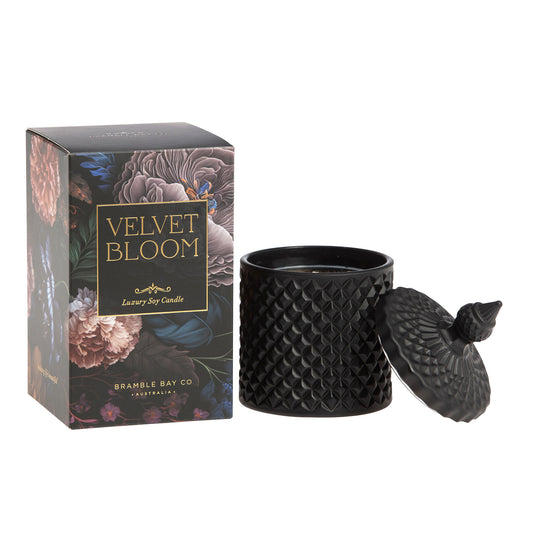 A black, textured Bramble Bay Co scented candle with a geometric pattern, accompanied by its packaging that features floral artwork and the name 'Velvet Bloom'.