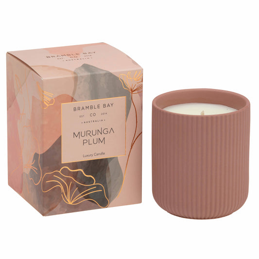 A Bramble Bay Co Murunga Plum terracotta ceramic candle vessel with a candle inside, next to its packaging that features abstract designs and the product name 'Murunga Plum'.