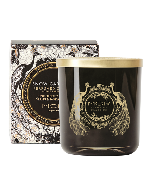 A MOR deluxe soy candle with a black wax and gold embellishments, hand poured into a gold rimmed glass vessel with a decorative lid, presented with a box packaged in black and white floral patterned paper.