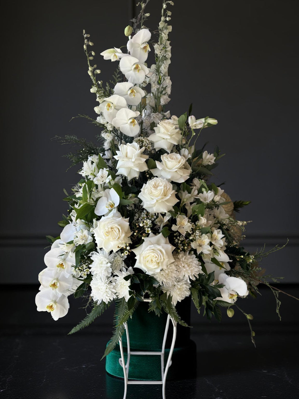 White funeral arrangement featuring cascading orchids, roses, chrysanthemums, and lush greenery in a standing display