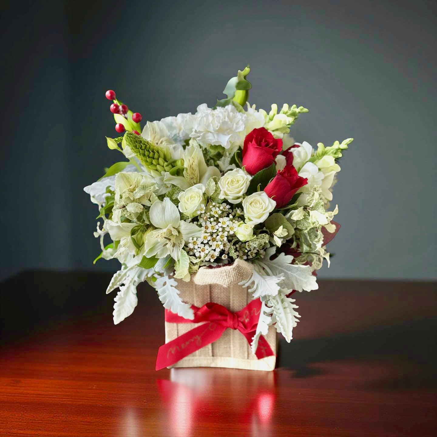 Fresh red and white Christmas flower arrangement in a hessian gift bag with a red Merry Christmas ribbon.