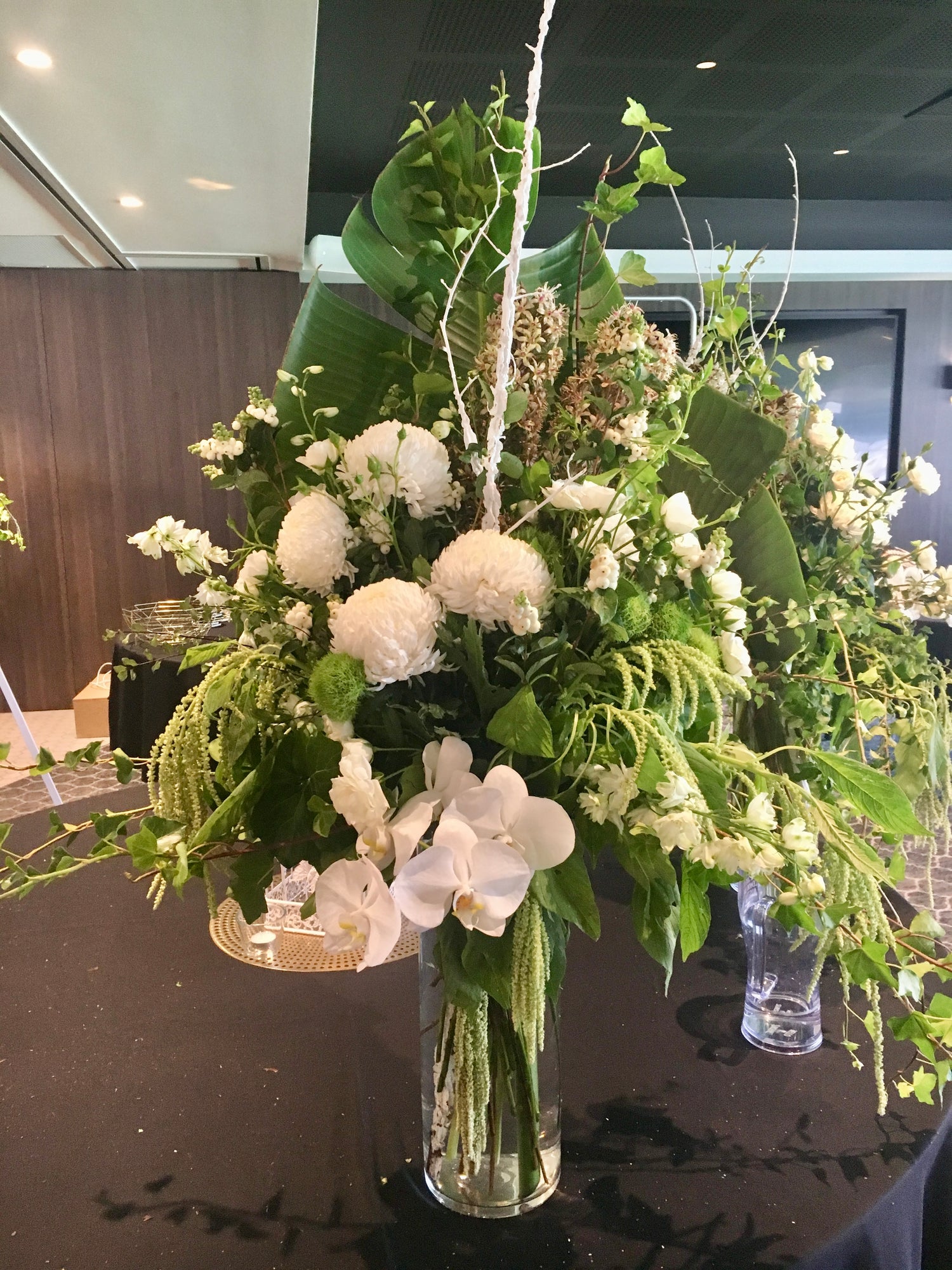 A photograph displaying three luxurious floral arrangements with a predominance of white flowers and green foliage, arranged in clear vases, intended for event decor.