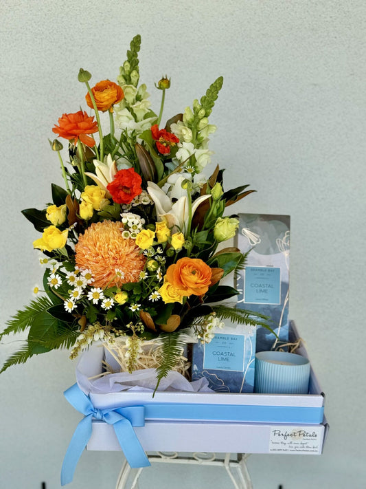 A gift hamper box with a vibrant floral arrangement in yellow and orange hues, accompanied by a Bramble Bay Co Coastal Lime scented candle and a fragrance diffuser.