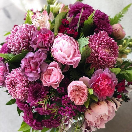 A pink bouquet featuring a variety of flowers including roses and carnations, with a mix of blueberry, mulberry, and strawberry tones.