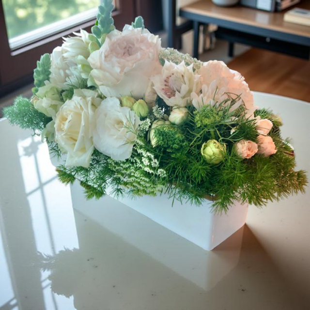 A floral centerpiece with a mix of white and pink blooms including blushing bride, lissianthus, cottage roses and lush greenery, arranged in a long, rectangular white container.