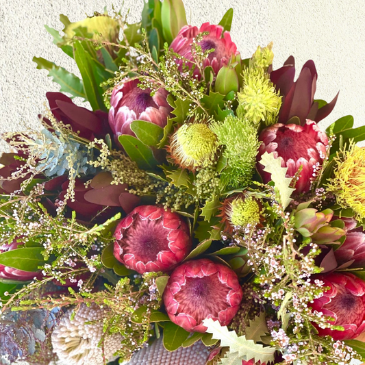 A bouquet of Australian native flowers featuring a variety of colors and textures, predominantly in shades of green and purple.