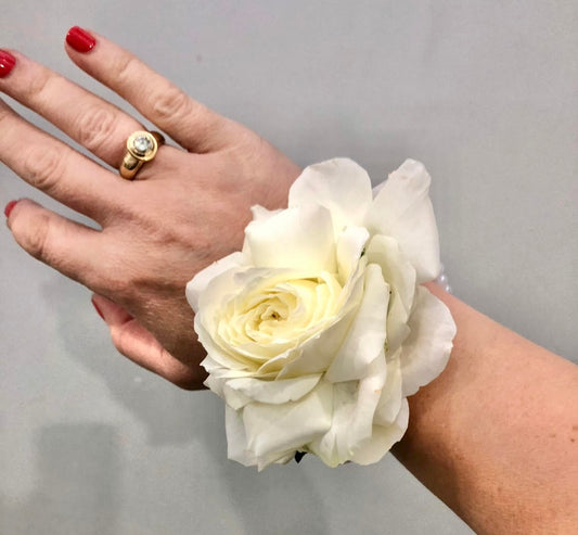 A hand wearing a bespoke wrist corsage featuring a single white rose.