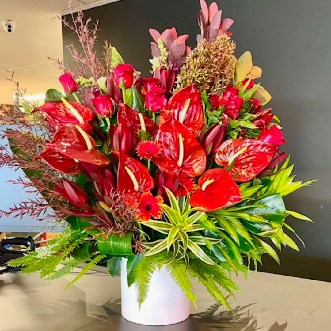 A floral arrangement featuring a mix of red and green foliage, with prominent red roses and other flowers in a white vase.