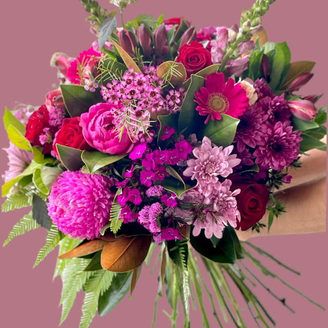 A vibrant bouquet featuring a lively palette of fuchsia, deep magenta, and bold crimson blooms with lush greenery.