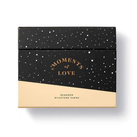 A black and gold baby milestone cards box with the title 'Moments of Love' and 'Newborn Milestone Cards' written on it.