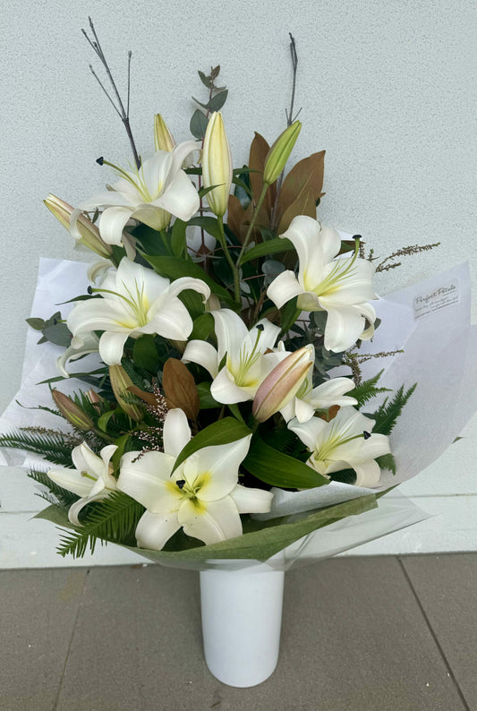 A bouquet of white oriental lilies arranged in a vase with green foliage.