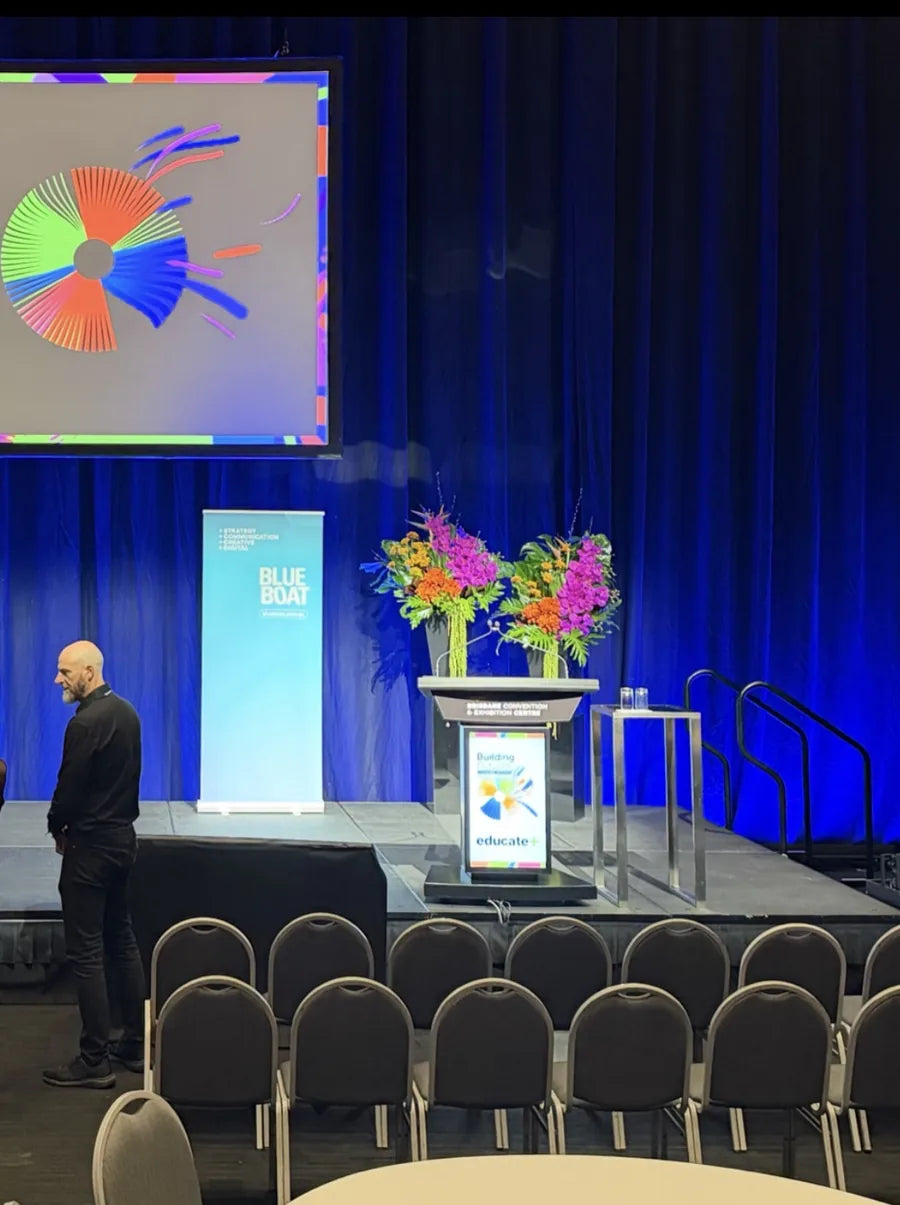 A conference stage at the Brisbane Convention and Exhibition Centre with two tall tropical floral arrangements beside the lectern