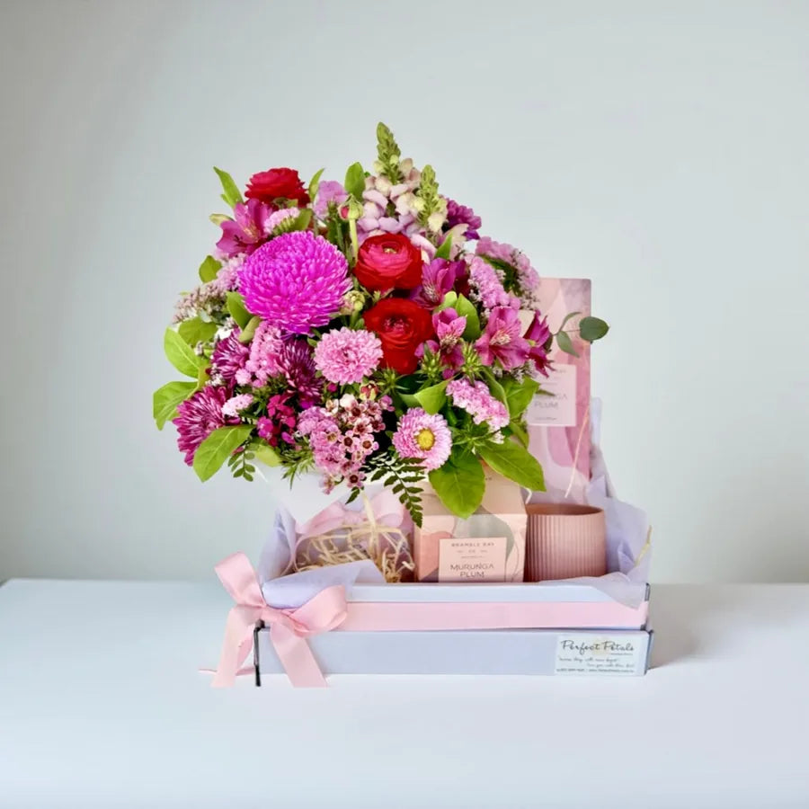 A gift hamper set including a bright pink flower arrangement, a Bramble Bay Co Murunga Plum scented candle, and a fragrance diffuser, all presented in a box with a pink ribbon.