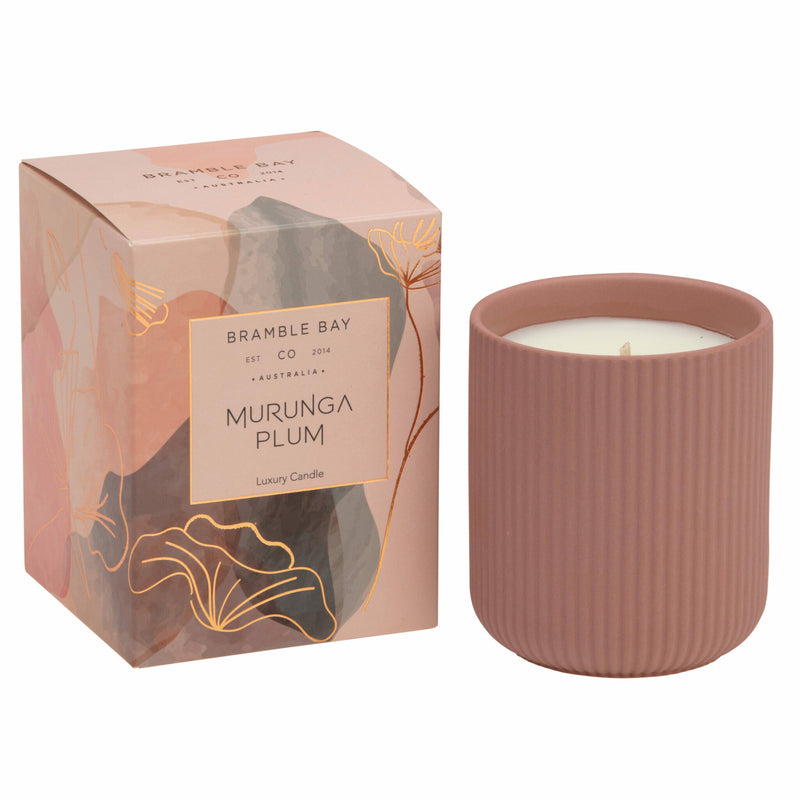 A Bramble Bay Co Murunga Plum terracotta ceramic candle vessel with a candle inside, next to its packaging that features abstract designs and the product name 'Murunga Plum'.