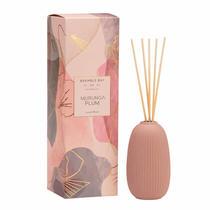 A Bramble Bay Co. Murunga Plum ceramic diffuser in a terracotta vessel with abstract pink and bronze packaging, alongside its pink box with floral designs.