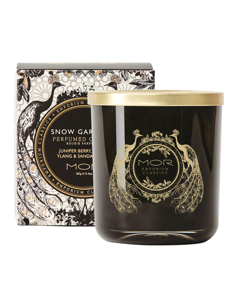 A MOR deluxe soy candle with a black wax and gold embellishments, hand poured into a gold rimmed glass vessel with a decorative lid, presented with a box packaged in black and white floral patterned paper.