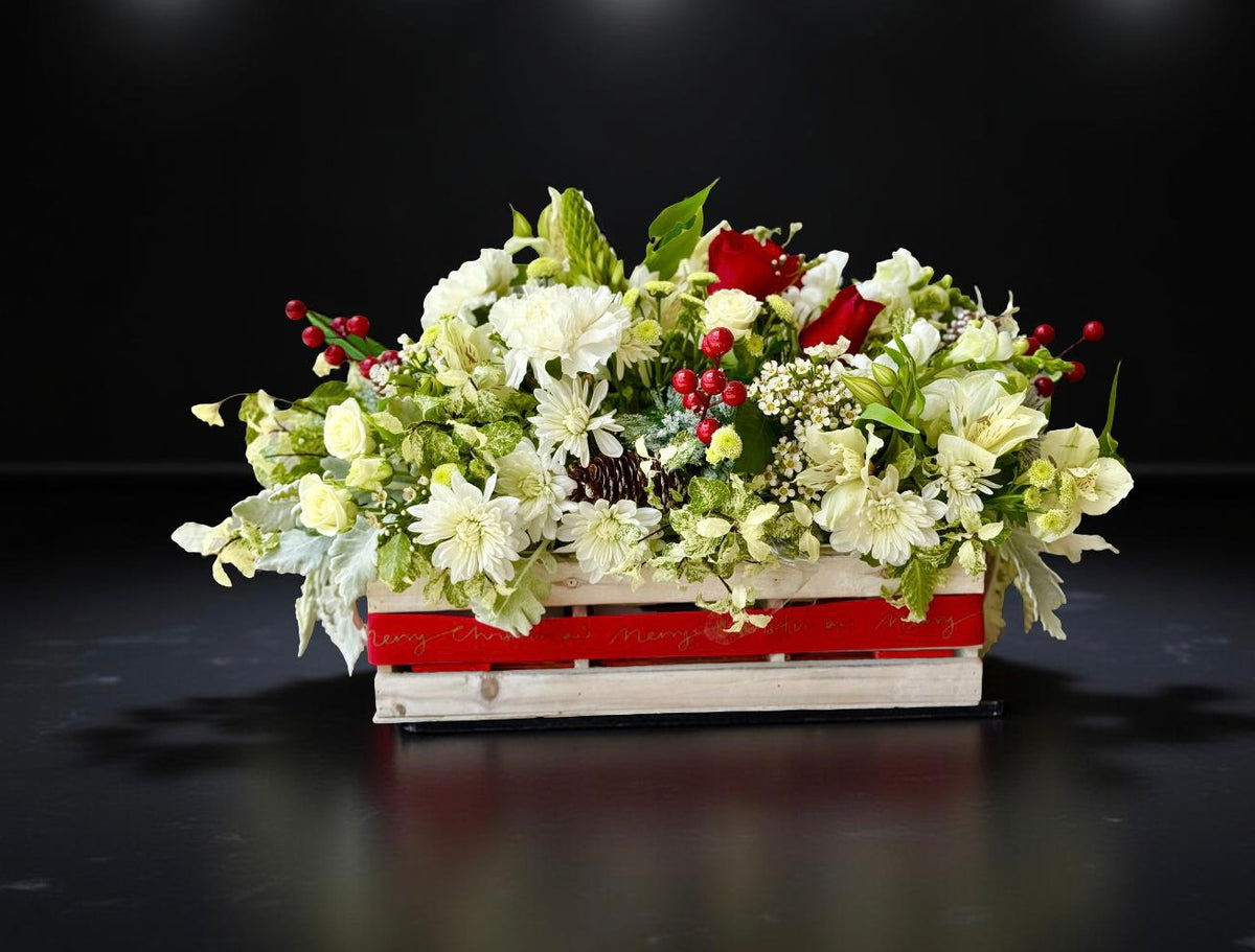Fresh red, white and green Christmas flower table centrepiece arranged in a reusable wooden crate.