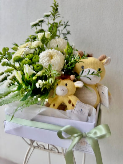 Newborn baby gift hamper including white floral arrangement with Living Textiles Noah the Giraffe cuddle toy and matching rattle.