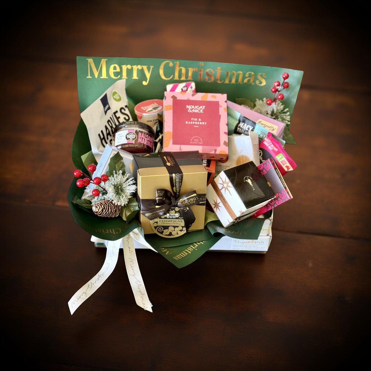 Gift basket with various items on a wooden surface, featuring a 'Merry Christmas' card.