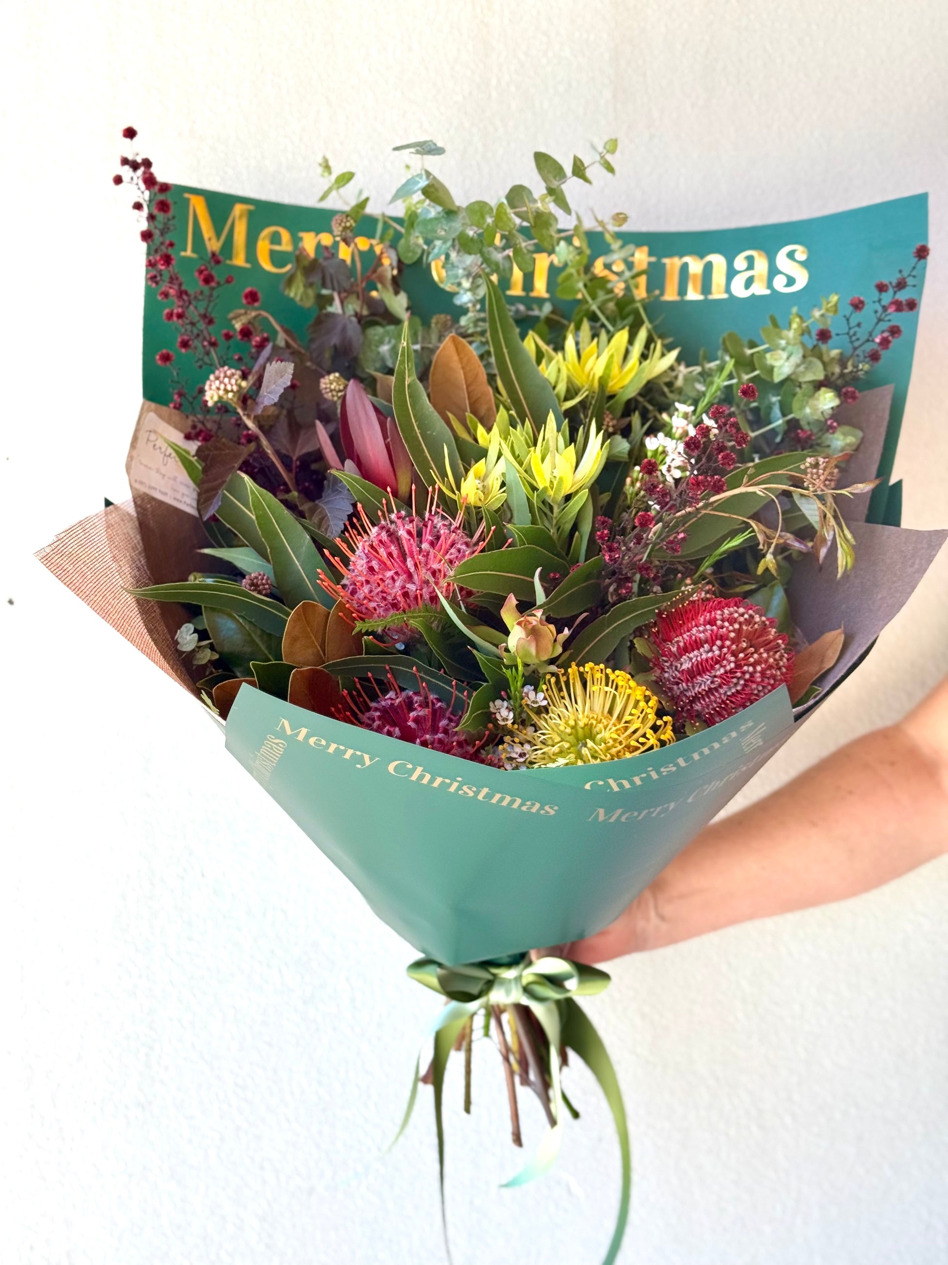 Bouquet of flowers wrapped in green paper with 'Merry Christmas' text on a white background