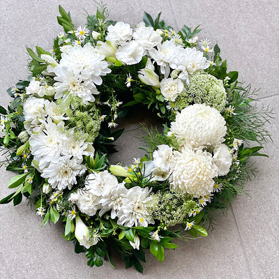 A floral sympathy wreath with predominantly white flowers and green foliage.