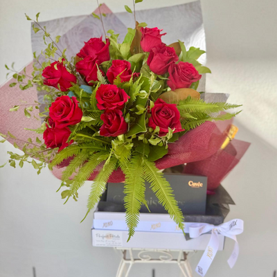 A gift set including a bouquet of red roses and a box of chocolates and a bottle of gold prosecco.