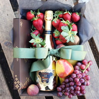 A gourmet hamper basket containing an assortment of fresh fruits, including strawberries, grapes, and a bottle of sparkling wine and chocolates, all elegantly arranged on a wooden surface.