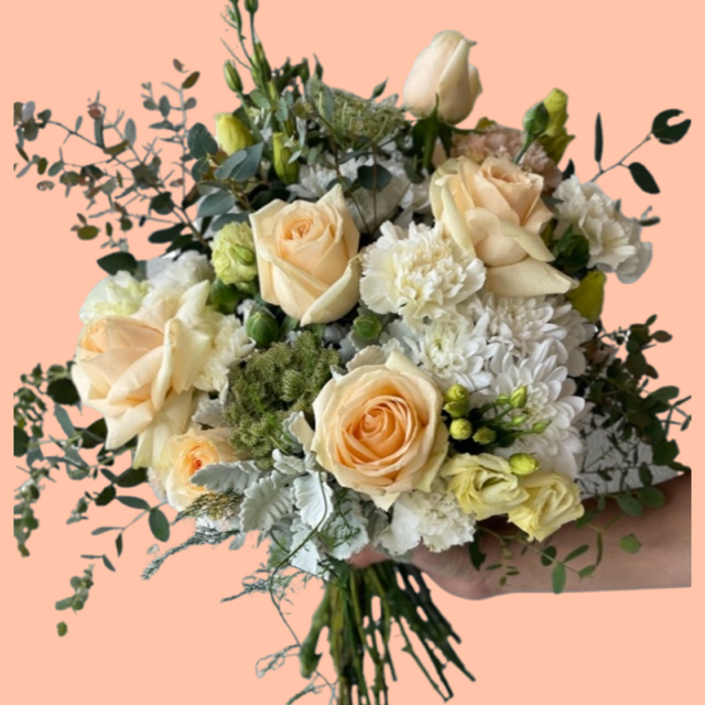 A bouquet of flowers featuring peach roses, creamy white blooms, and soft greenery.