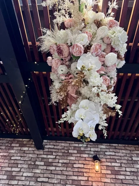 A cascading silk floral installation in blush and white, with peonies, roses and phalaenopsis orchids, mounted on a dark timber gate